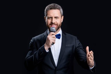 Siyah arka planda izole edilmiş mutlu smokin adam sunucusu. Stüdyoda sunucu. Mikrofonlu smokin adam sunucusu. Smokinli sunucunun fotoğrafı. Mikrofon..