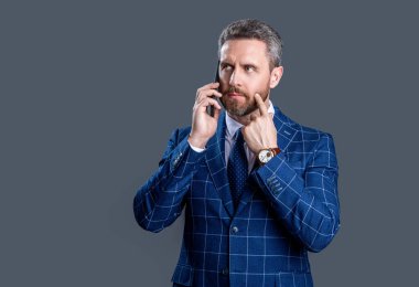 Düşünen iş adamı stüdyoda telefonla konuşuyor. İş adamının telefonda konuştuğu fotoğraf. İş adamı telefonda takım elbiseli konuşur. Gri arka planda izole iş adamı konuşması.