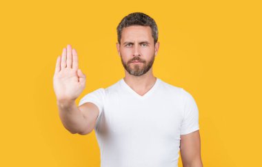 Duran ve stüdyoda jest yapmayan bir adam. Stop Man 'in fotoğrafı göstermiyor. Durmadan hareket eden bir adam. Tişörtlü sakallı adam dur diyor ve sarı arka planda izole edilmemiş..