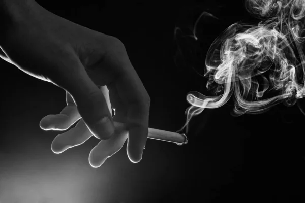 男性の手は煙の渦と燃えるタバコを保持暗い背景 喫煙習慣 — ストック写真
