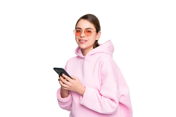 stock image Happy young woman in casual pink hoodie and glasses using mobile phone isolated on white, millennial.