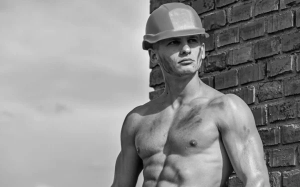 stock image Builder with muscular torso and helmet, brick wall and sky on background. Athlete with nude torso in hard hat, copy space. Builder with strong muscular body covered with dust. Sexy builder concept.