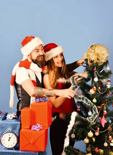 モミの木の近くに赤と青の贈り物を持つミスターとミッシークラウス クリスマスの贈り物と愛の概念 サンタとセクシーな女の子が一緒にクリスマスツリーを飾る 青い背景に幸せな顔をした男と女 — ストック写真
