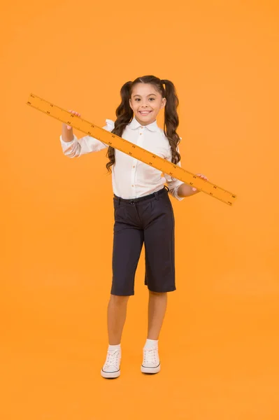 Learning geometry at school. Small school child holding measuring device on yellow background. Little girl preparing long wooden ruler for school lesson. Keep measuring and back to school.