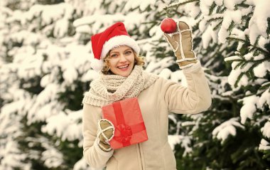 Ne güzel bir sürpriz. Beyaz karla kaplı kış ormanı. Açık hava mükemmel bir ruh halidir. Mutlu kadın hediye kutusunu tutar. Noel ağacı süslemeli kız. Bayan Kırmızı Noel Baba şapkası kürk ağacında.