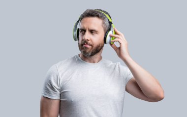 Yakışıklı adam stüdyoda kulaklıkla müzik dinliyor. Adam modern kulaklıkla müzik dinliyor. Kulaklıkla müzik dinleyen bir adamın fotoğrafı. Adam kulaklıkla müzik dinliyor. Gri arka planda izole edilmiş..