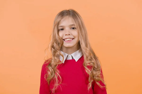 毛茸茸的金发 穿着红色毛衣的孩子 女孩在橙色的背景下微笑 孩子的时尚和风格 快乐童年的概念 — 图库照片