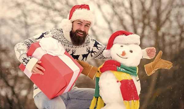 友達だ 冬の活動 メリークリスマス サンタは屋外でプレゼントする Xmasの準備ができて幸せなヒップスター 冬休みだ 寒い日の暖かいセーター 髭を生やした男が雪だるまを作り — ストック写真