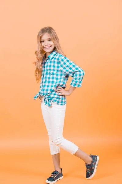 孩子模型微笑与长的金黄头发 穿格子衬衫 橙色背景运动鞋的女孩 孩子的时尚 快乐的童年概念 — 图库照片