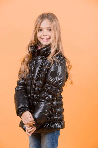 子供の美しさ 長いブロンドの髪を持つ子モデル笑顔 ファッション 秋スタイル トレンド 幸せな子供時代のコンセプトです オレンジ色の背景に黒のコートを着た少女 — ストック写真
