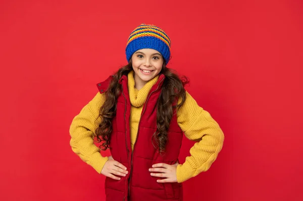portrait of child wearing warm clothes. express positive emotion. winter fashion. positive kid with curly hair in hat. female fashion model. teen girl in down vest.