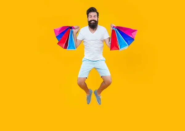 cheerful man jumping in studio with bags. shopping sale concept. shopping sale of jumping man isolated on yellow background. jumping man on shopping sale. bearded man go shopping at sale.