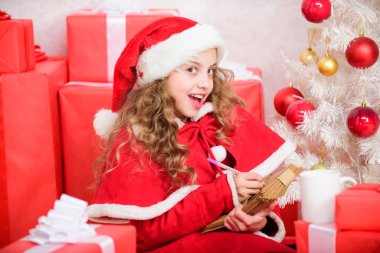 Küçük kız elinde kalem ve kağıt ile Noel ağacı yakınında mektup yazıyor. Çocuk Noel Baba 'ya mektup yazmış. Mucizeye inan. Noel Baba 'ya mektup. Dilek listesi. Çocuk Noel Baba kostümü afiyet olsun..