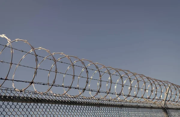 stock image barbwire perimeter fence. ensuring safety and security. jail wall. highly protected prison wall with barbed wire fence. steel grating fence. coiled razor wire with its sharp steel barbs.