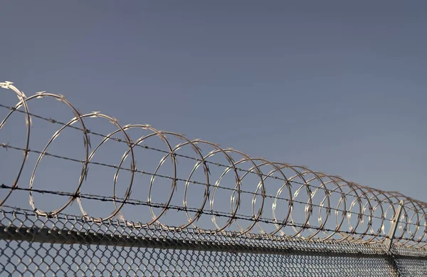 Stock image barbwire perimeter fence. ensuring safety and security. jail wall. highly protected prison wall with barbed wire fence. steel grating fence. coiled razor wire with its sharp steel barbs.