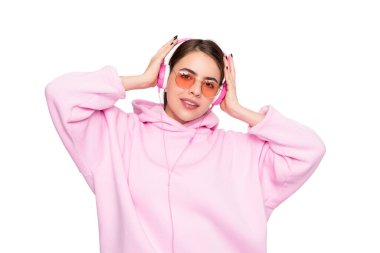 Pembe kapüşonlu ve gözlüklü mutlu kız beyaz kulaklıkla müzik dinlemekten zevk alıyor..