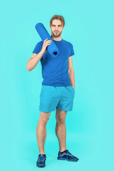 sport man with yoga mat standing in studio. photo of sport man with yoga mat. sport man with yoga mat wearing sportswear. sport man with yoga mat isolated on blue background.