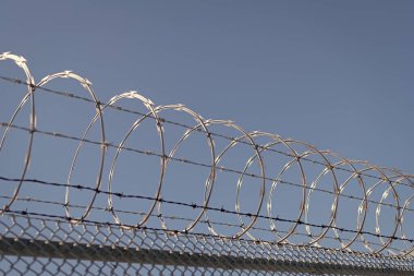 Hapishane duvarı. Dikenli tel örgülü yüksek korumalı hapishane duvarı. Çelik parmaklıklar. Sivri çelik dikenli tellerle sarmalanmış tel örgü çitlerin tepesinde. Güvenlik ve güvenliğin sağlanması.
