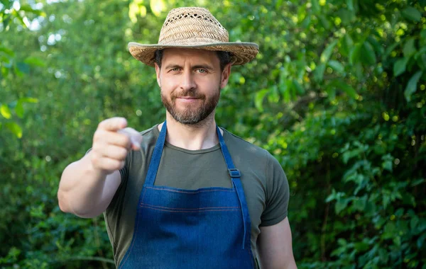 Happy farmer man in farmers hat and apron pointing finger forward natural outdoors.
