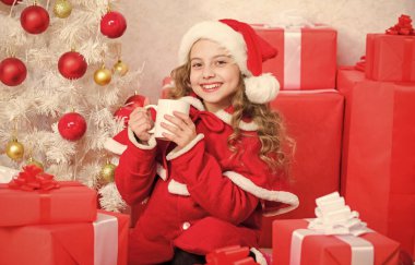 Çocuk Noel Baba şapkası kakao içeceğinin tadını çıkarıyor. Tatil sezonunu ısıtmak için mükemmel bir yol. Noel arifesinde sıcak kakao. Kakao en sevdiği içecek. Küçük tatlı kız Noel 'i kutlarken sıcak içecekle bardağı tutuyor..