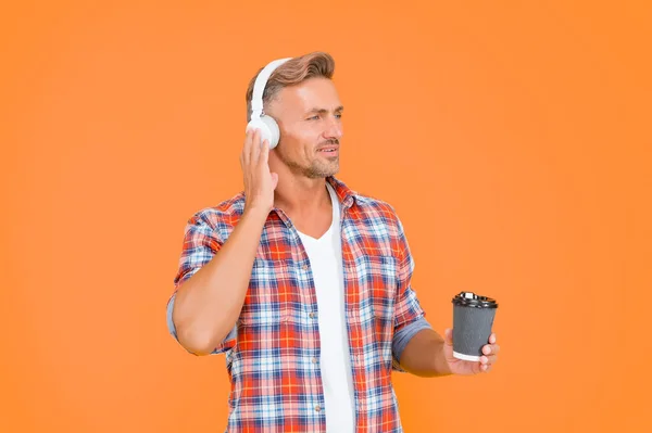 Middle-aged caucasian man listen to music in earphones holding hot coffee cup, break time.