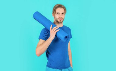 Stüdyoda yoga minderli bir sporcu. Yoga minderli bir sporcunun fotoğrafı. Spor giyimli yoga minderli bir sporcu. Yoga minderli sporcu mavi arka planda izole edilmiş..