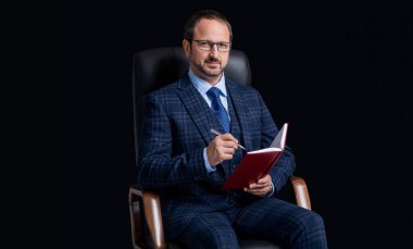 Adam ofis sandalyesinde planlama tutmuyor. Planlamacı, adamın elinde not tutuyor. Planlama yapan adamın fotoğrafı. Planlayıcısı olan adam siyah arkaplanda izole edildi.