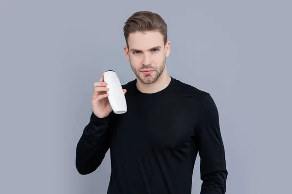 man with bristle hold aftershave product isolated on grey background. man with aftershave product in studio. aftershave product for man. handsome man hold bottle of aftershave product.