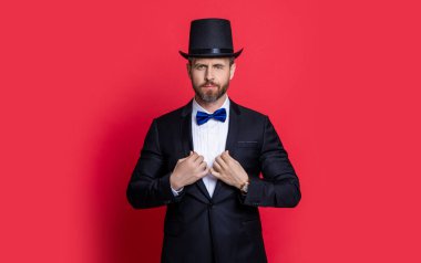 Silindir şapkalı sihirbaz. Erkek sihirbaz stüdyoda smokin giyer. Silindir şapkalı sihirbaz. Adam sihirbaz kırmızı arka planda izole.