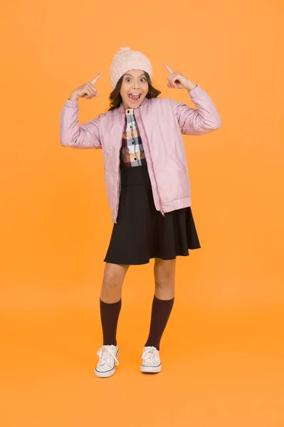 Crazy idea. Happy child yellow background. Warm clothes for cold season. Fashionable girl looks like hipster. Small girl winter hat. Trendy schoolgirl wear jacket skirt and long socks. Clothes shop.