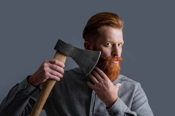 斧を持った赤い髭の床屋の男のスタジオショット 理容室のコンセプト 赤い髭の男床屋は灰色の背景に斧を隔離している 斧を持つ理髪師は赤い髭を生やし — ストック写真