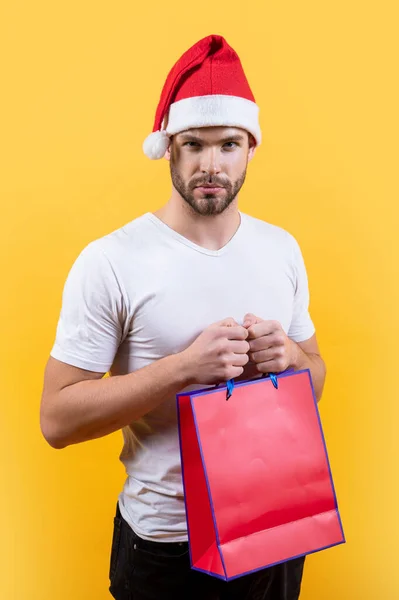 メリー クリスマス サンタ ハットの若い男がクリスマス ショッピングバッグを持ってる スタジオに赤いクリスマスの買い物袋を持った男 黄色の背景に隔離されたクリスマス休暇のサンタさん — ストック写真