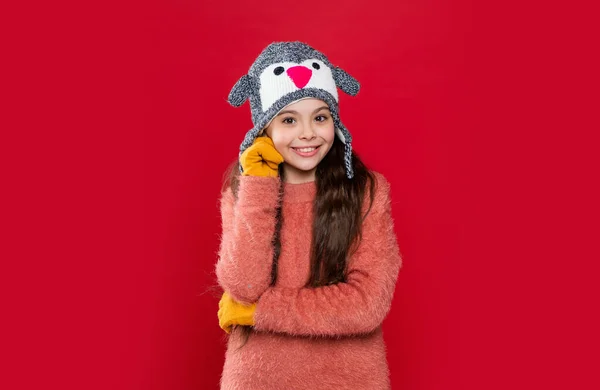 winter fashion for happy teen girl. teen girl fashion model in winter earflap hat. teen girl in winter fashion hat isolated on red. teen girl wear sweater and winter fashion hat in studio.