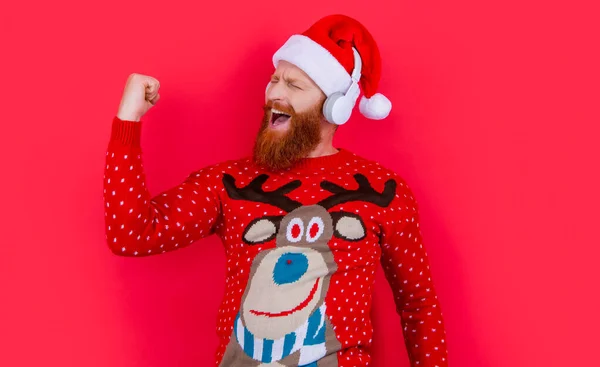 xmas music. cheerful bearded man celebrate xmas with music. man in headphones listen xmas music isolated on red background.