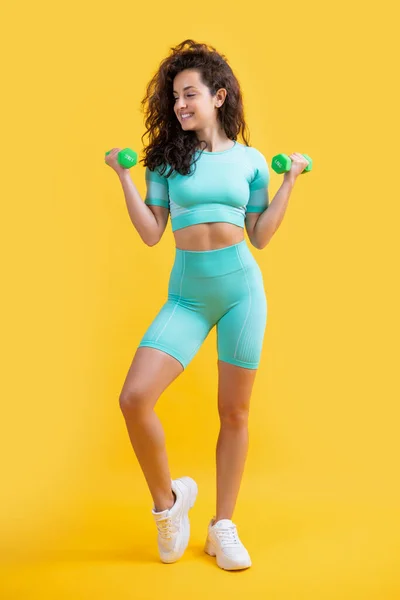 smiling fitness woman do weightlifting exercise with dumbbell in studio. fitness woman do weightlifting exercise isolated on yellow background. fitness and sport.