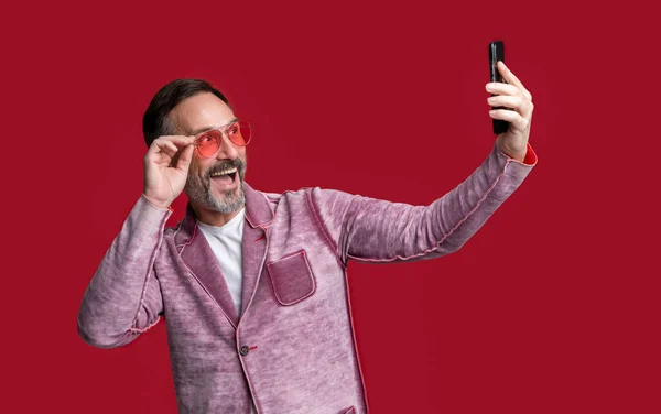 phone blogging of amazed selfie man. photo of selfie man blogging on phone. stylish man blogging on phone isolated on red background. man make selfie for phone blogging in studio.