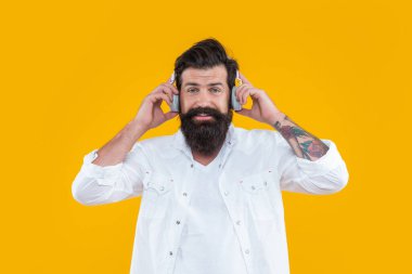 Gülümseyen hippi adam sarı arka planda izole edilmiş kulaklıklarla dinleme defteri. Kulaklıkla kitap. Dinleme kitabı için kulaklık takan bir adam. Müzik dinlemek için kulaklık tutan hipster 'ın stüdyo fotoğrafı..