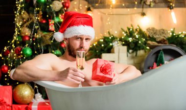 Kış tatili Noel konsepti. Küvette yatan adam hediye kutusuyla rahatlar. Spa ve sağlık. Sıcak banyo. Sıcak banyo sağlık yararları. Noel Baba sıcak banyoda lüks içinde. Keyfini çıkar. Kendimi şımartıyorum..