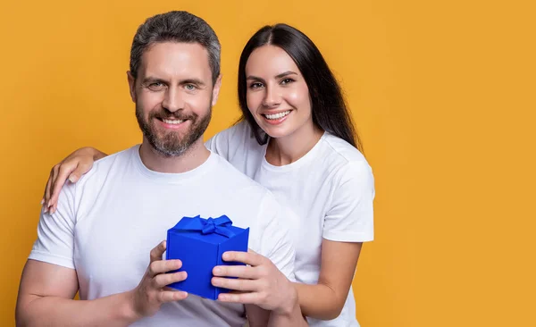 stock image glad holiday couple with present box. photo of couple with present for holiday surprise. mens day. couple with surprise present isolated on yellow background. surprise couple with present in studio.