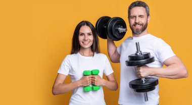 Spor salonunda halterli, fotokopi alanı olan spor ayakkabılı bir çift. Halterli spor çifti fotoğrafı. Halterli spor çifti sarı arka planda izole edilmiş. Stüdyoda halterli fitness çifti.