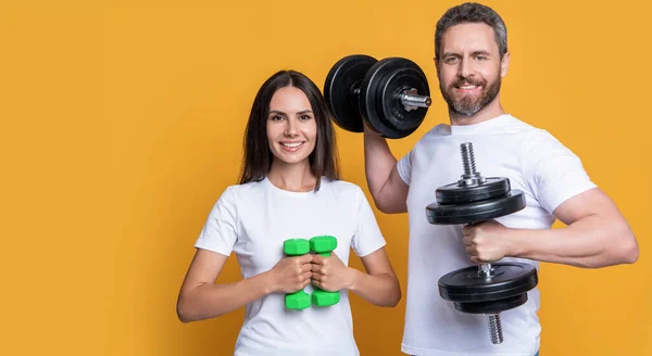 fitness couple with barbell in gym with copy space. photo of fitness couple with barbell. fitness couple with barbell isolated on yellow background. fitness couple with barbell in studio.