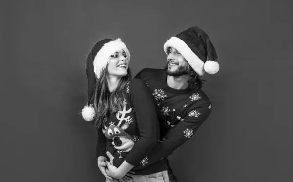 christmas time. happy new year couple in knitted sweater and santa claus hat. prepare for xmas party fun. happy holidays for young family. man and woman on red background. love.