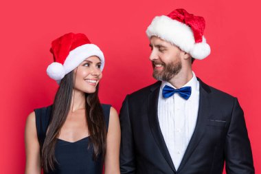 Stüdyodaki gülümseyen Noel Baba çiftimize mutlu Noeller. Noel Baba çifti için Noel kutlaması. Noel Baba şapkalı çift kırmızı arka planda izole edilmiş. Noel Baba çifti için kurumsal Noel partisi.