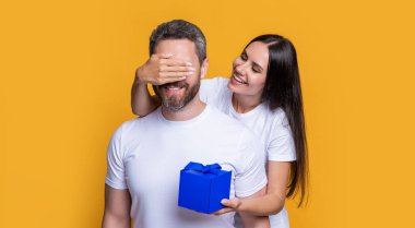 Kutusu olan neşeli bir tatil çifti. Bayram sürprizi için hediyeli bir çift fotoğrafı. Erkekler günü. Sarı arka planda sürpriz hediyeli çift var. Sürpriz çift.