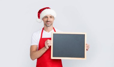 Noel Baba şapkalı ve önlüklü olgun bir adam fotokopi alanı olan karatahtayı tutuyor..