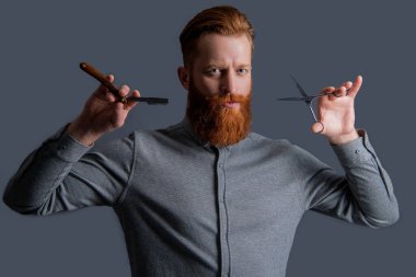 Berber dükkanında elinde makas olan traşsız bir adam. Berber dükkanındaki berber. Berber adam kuaförde makas ve bıçak tutuyor. Berber dükkanı konsepti. Berber adam gri arka planda izole edilmiş..