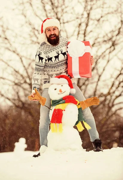 驚きのコンセプト 冬の試合だ 冬のアクティビティ 冬休み 男幸せな顔雪の性質の背景 髭を生やしたヒップスターはギフトボックスを保持します 男は雪だるまを作った 男サンタ帽子楽しい屋外 — ストック写真