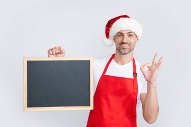 Noel Baba şapkalı ve önlüklü mutlu olgun adam fotokopi alanı olan tahtayı tutuyor. Tamam.