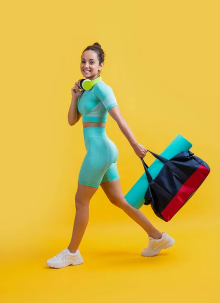 smiling fitness sportswoman in sportswear walk with sport bag in studio. fitness sportswoman in workout sportswear isolated on yellow background. fitness and sportswear.