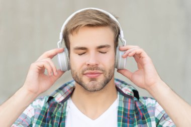 Müzik dinlemekten ve kareli gömlek giymekten hoşlanan bir adam. Kulaklıkla müzik dinleyen bir adamın fotoğrafı. Dışarıda müzik dinleyen bir adam. Adam dışarıda müzik dinliyor..